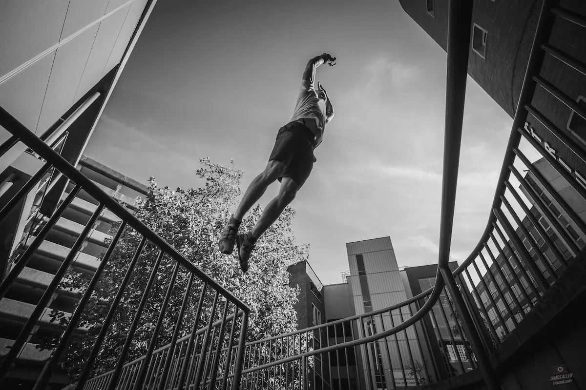 Frankie in the middle of a jump between railings, practising Parkour.